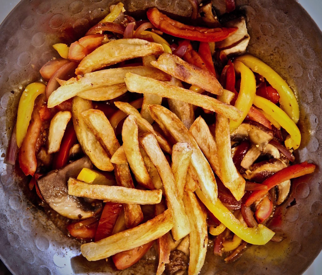 French fries being added to mushroom saltado.